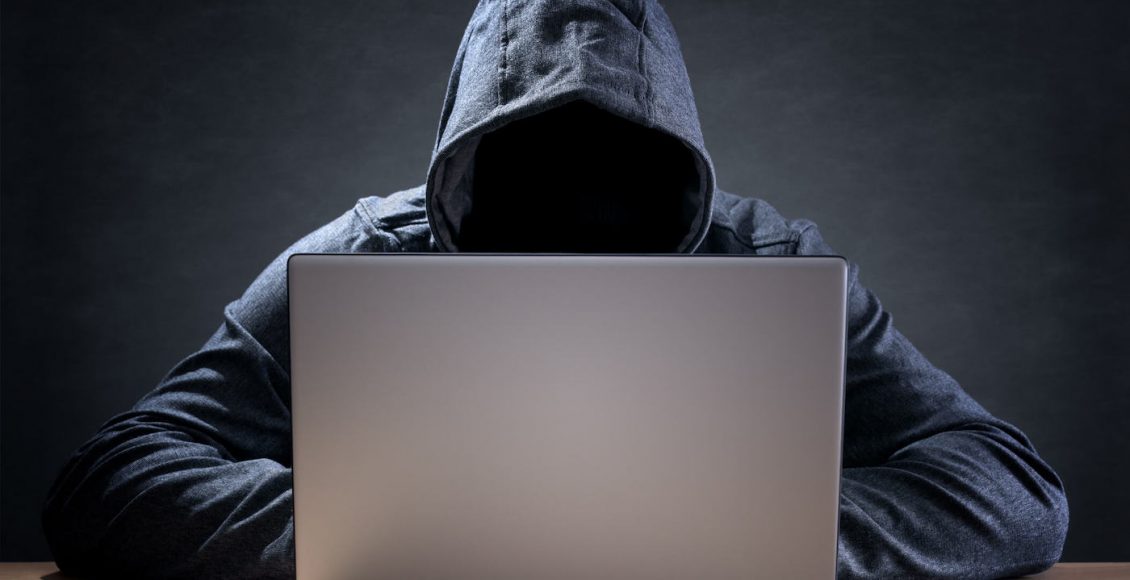 Person-Wearing-A-Gray-Hoodie-With-Face-Hidden-Typing-On-Computer